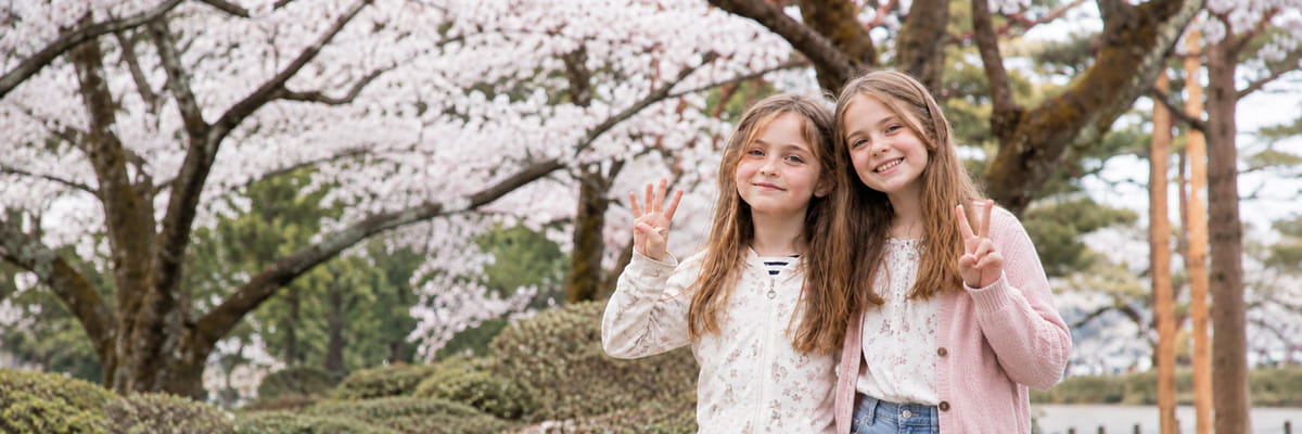 Families with Teens - Teenage siblings admiring cherry blossom canopy along a scenic Japanese river in spring