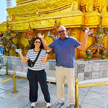 Couple exploring a traditional Thai temple with golden pagoda in Thailand